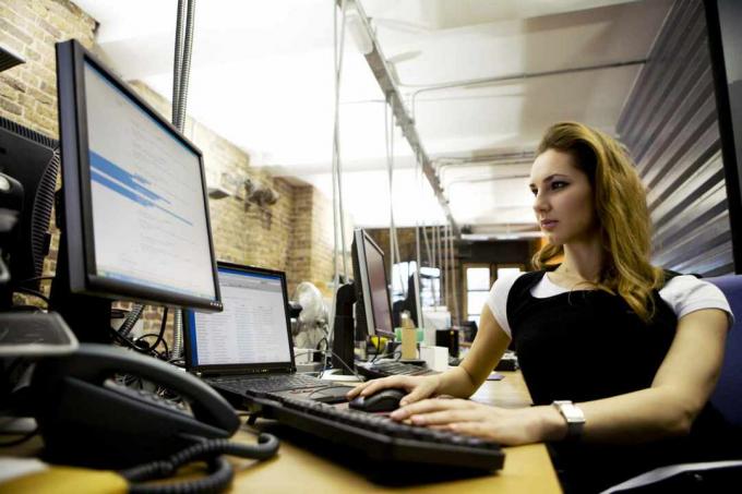 Moteris, sėdinti prie stalo, naudodama nešiojamąjį kompiuterį su išorine klaviatūra ir monitoriumi.