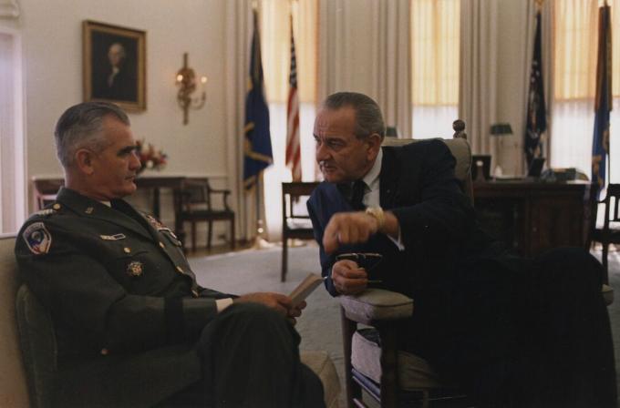 JAV kariuomenės uniformoje ir sėdintis generolas Williamas Westmorelandas kalba su prezidentu Lyndonu B. Džonsonas ovaliniame kabinete.