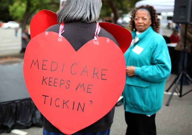 Moteris dėvi širdies formos ženklą su užrašu „Medicare Keeps Me Ticking“