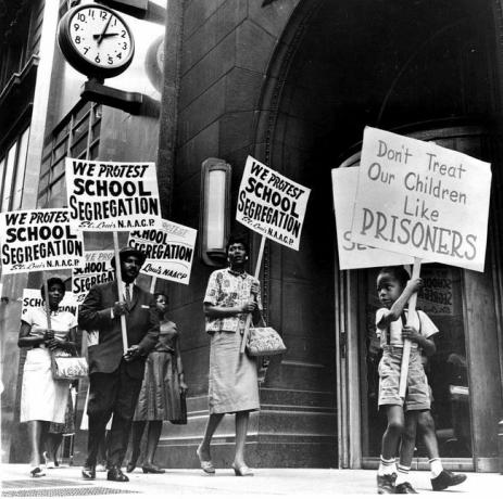 Demonstrantai, tarp jų ir jaunas berniukas, protestuodami prieš segregaciją piketuoja prie mokyklos tarybos biuro.