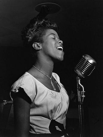 Sarah Vaughan dainuoja į mikrofoną, nespalvota nuotrauka.